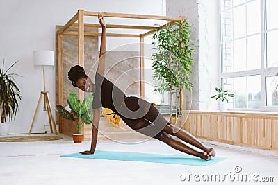 Laughing, smiling multicultural woman do yoga exercises on mat. Practicing Vasisthasana side plank with one arm indoors Stock Photo