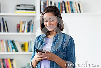 Laughing spanish young adult woman sending message with mobile phone Stock Photo