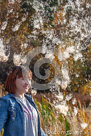 A laughing teenage girl of European appearance stands under the falling fluff from a cattail. Stock Photo