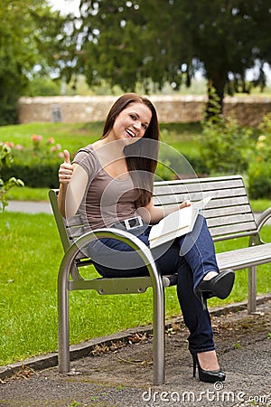 Laughing woman with book posing thumbs up Stock Photo