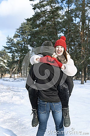 Laughing woman keeps hands in heart shape sign sitting on her guy hands. Young loving couple in winter forest Stock Photo