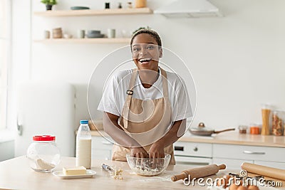 Laughing young african american lady in apron making pie dough in minimalist kitchen interior Stock Photo