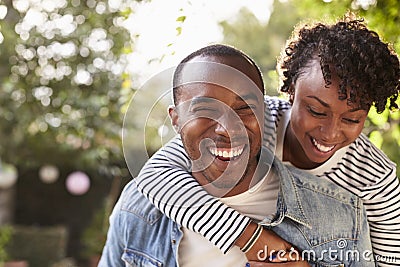 Laughing young black couple piggyback in garden, to camera Stock Photo