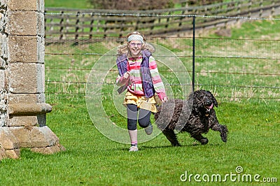 Laughing young girl running with black labradoodle dog in a rural setting Stock Photo