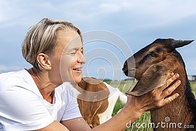 Laughing young woman in a white tank top with a goat in a field. Love and tenderness for animals and nature. Close-up Stock Photo