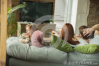 Family spending nice time together at home, looks happy and cheerful, watching TV Stock Photo