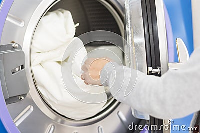 Laundry washing machine. A hand putting or getting some bed sheets from or into the laundry washing machine. Stock Photo