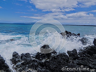 Lava Rock and Coral with Spray of crashing wave in tide pools at Maluaka Beach and Kihei Maui with sky and clouds Stock Photo