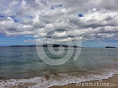 Lava Rock and Coral with Spray of crashing wave in tide pools at Maluaka Beach and Kihei Maui with sky and clouds Stock Photo