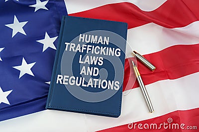 On the US flag lies a pen and a book with the inscription - HUMAN TRAFFICKING LAWS AND REGULATIONS Stock Photo
