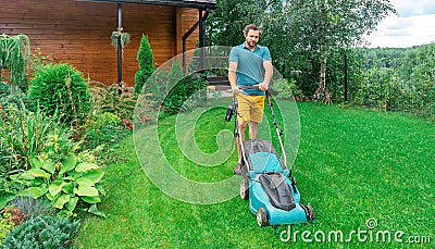 Lawn care. Mowing grass with an electric lawn mower. A young man mows the grass with a lawn mower with a grass collector on a Stock Photo