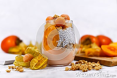 Layered healthy breakfast in glass with chia seeds pudding, mixed with granola and topped with orange persimmon and physalis fruit Stock Photo