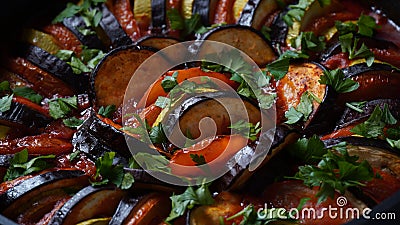 Layered ratatouille in a baking dish, slices of zucchini, red bell pepper, chili, yellow squash, eggplant, olive oil, parsley and Stock Photo