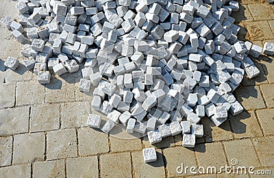 Laying granite and marble light, white gray, medium size cubes. tilers put cobblestones in sand or gravel. they have piles ready t Stock Photo