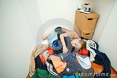 Lazy boy sleeping on the pile of thrown clothes. Mess in open wardrobe. Untidy clutter clothing closet Stock Photo