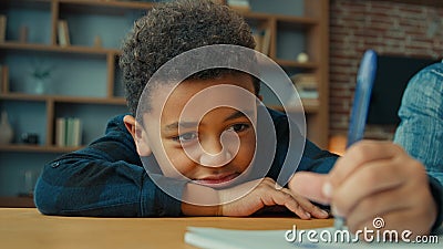 Lazy unmotivated tired exhausted fatigued little African American pupil schoolboy writing notes doing homework lying on Stock Photo