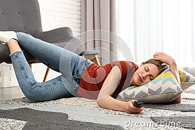 Lazy young woman with TV remote sleeping on floor at home Stock Photo