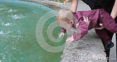 Le bébé chanceux essayant de toucher l'eau dans la fontaine dans le mouvement lent, mère tient son fils près de l'eau banque de vidéos Le bébé chanceux essayant de toucher l'eau dans la fontaine dans le mouvement lent, mère tient son fils près de l'eau banque de vidéos