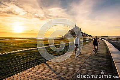 A couple of tourists biking at sunset towards the Mont Saint-Michel tidal island in Normandy, France Editorial Stock Photo