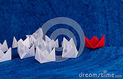 Leadership concept shown using white paper boats wandering in the sea and one red boat on track Stock Photo