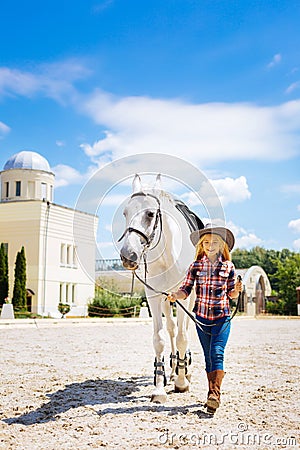 Amused schoolgirl leading white horse on race track Stock Photo