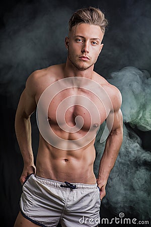 Lean athletic shirtless young man standing on dark background Stock Photo