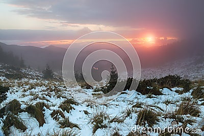 From the lean covered by snow there is a view opened to the mountains, morning fog and sunset. Sun rays lighten up the sky. Stock Photo
