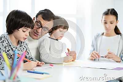 Learning process. Adorable little latin boy drawing something while spending time with his father and siblings at home Stock Photo
