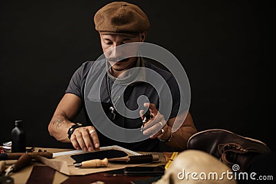 Whiskered shoemaker with making measurments in patterns at table in workshop Stock Photo