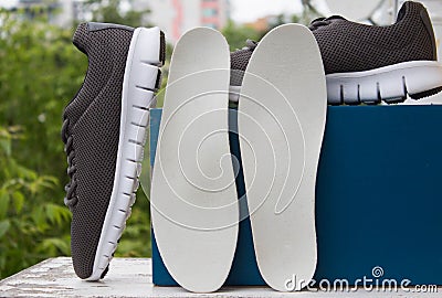 Leather orthopedic insoles in front of blue box and pair of sport shoes. Outdoors Stock Photo