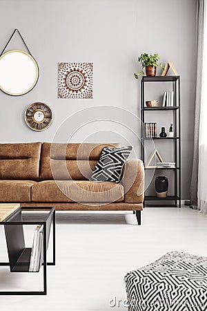 Leather sofa with black and white pillow in real photo of sitting room interior with metal rack with books, decor and fresh plant Stock Photo