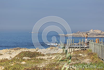 View of woman taking pictures on pedestrian wooden walkway, beach and sea as Editorial Stock Photo