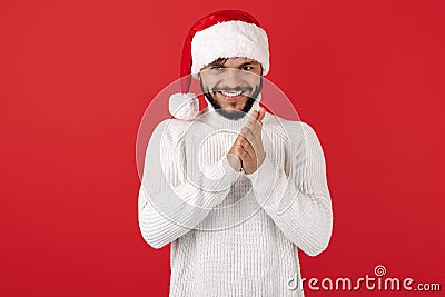 Leery hipster man wears santa claus hat over red background. Christmas and New Year concept. Stock Photo