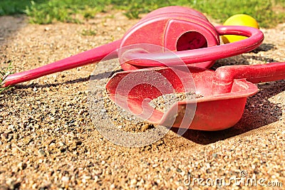 Left children toys on the sand. Red watering can, shovel and yellow ball. Stock Photo