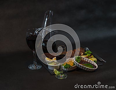 left side view on a rack of pork ribs with potatoes, sauces, bread and red wine in a carafe and glass, the second glass of liqueur Stock Photo
