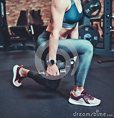 Leg muscle training, lunges with dumbbells. Athletic model woman with sports body exercising with dumbbells in the gym. Stock Photo