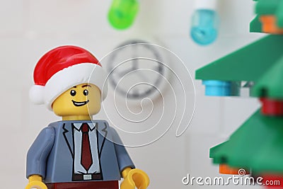 A Lego businessman minifigure wearing a Santa hat and standing next to a Christmas tree in his office Editorial Stock Photo