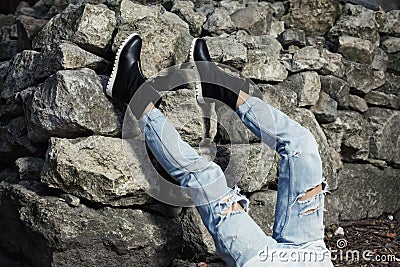 Legs dressed in ripped blue jeanswith black stylish boots. Studio photo on rock wall background Stock Photo