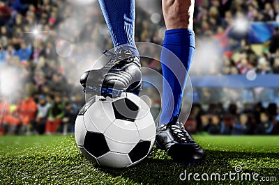 Legs and feet of football player in blue socks and black shoes standing with the ball playing match at soccer stadium Stock Photo