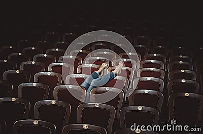 Legs of a girl in jeans are shown from behind the seats in the theater Stock Photo
