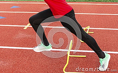 Sprinter performing running drill over yellow mini hurdle on a track Stock Photo