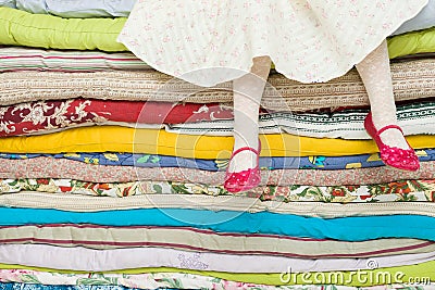 Legs of a little girl sitting on a pile of colorful mattresses. Decorations for the fairy tale The princess on a Pea Stock Photo