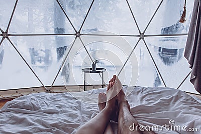 Legs of a man and woman couple in bed against the background of a snow-covered forest in a dome camping Stock Photo