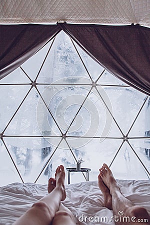 Legs of a man and woman couple in bed against the background of a snow-covered forest in a dome camping Stock Photo