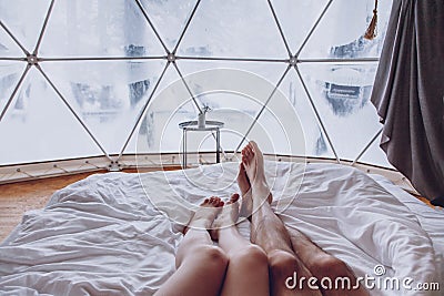 Legs of a man and woman couple in bed against the background of a snow-covered forest in a dome camping Stock Photo