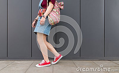 Legs in red sneakers, backpack and denim dresses go down the ground against the background of a dark wall Stock Photo