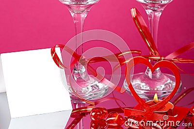 Legs of two champagne glasses with ribbons on a pink background and and a card and a heart candlestick with a burning candle Stock Photo