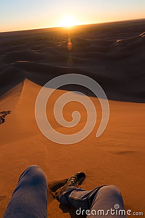 Legs of unrecognizable man from the top of a dune at sunrise, in Erg Chigaga, Morocco Stock Photo