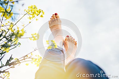 Legs up of happy female lying in deep yellow flowers meadow with bright sunny day optical sun beams flares. Happiness in nature Stock Photo