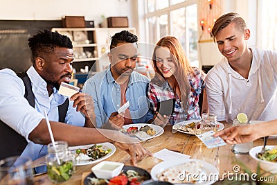 Happy friends with money paying bill at restaurant Stock Photo